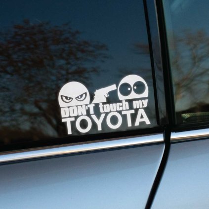 Plotrovaná nálepka s textom “Don’t touch my Toyota”, zamračená tvár so zbraňou mieri na udivenú tvár.