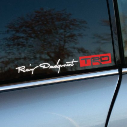 Biela a červená nálepka „Racing Development TRD“ je nalepená na tmavom bočnom okne strieborného auta. Elegantný rukopisný štýl nápisu „Racing Development“ dopĺňa moderný, výrazný červený štvorcový logotyp „TRD“, čo podčiarkuje závodnú DNA a prémiovú kvalitu. Kombinácia bieleho a červeného dizajnu na tmavom pozadí zaručuje výbornú viditeľnosť a pôsobí športovo aj profesionálne. Táto nálepka dokonale odráža vášeň pre tuning a pretekársky štýl, ideálna pre fanúšikov značky TRD a športových vozidiel.  Kľúčové slová: nálepka TRD, Racing Development, tuning nálepky, športové auto, autodoplnky, personalizácia auta, závodný dizajn.