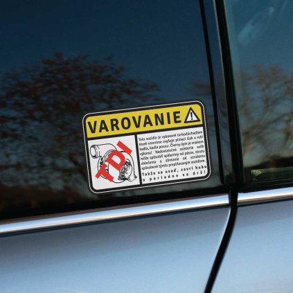 Vtipná nálepka s nápisom „Varovanie TDI“ na zadnom okne tmavosivého auta upozorňuje na výkonnosť vozidla vybaveného turbodúchadlom. Text v štýle výstražného označenia s humorným popisom o čiernom dyme a silnom zrýchlení jasne naznačuje, že toto auto nie je pre slabé povahy. Skvelý doplnok pre nadšencov dieselových motorov, ktorí chcú svojmu vozidlu dodať originálny a zábavný charakter, zatiaľ čo na cestách pobavia aj ostatných vodičov.