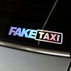 Plotrovaná nálepka s dúhovým holografickým efektom v hrubom písme a orámovaním textu v znení nápisu FAKE TAXI.