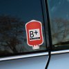 Tlačená nálepka v tvare krvného vaku s označením B+ Rh POSITIVE, určená na auto, prilbu alebo kufor pre rýchlu identifikáciu.
