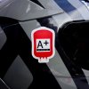 Tlačená nálepka v tvare krvného vaku s textom A+ Rh POSITIVE, ideálna na prilbu, kufor či auto pre rýchlu identifikáciu.