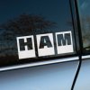 Na fotografii je biela nálepka s veľkými písmenami „HAM“ v jednotlivých štvorcoch, nalepená na bočnom okne auta. Tento minimalistický a výrazný dizajn môže odkazovať na automobilovú kultúru alebo byť hravou skratkou, ktorá vyvoláva zvedavosť. Nálepka dodáva autu osobitý charakter a je vhodná pre tých, ktorí sa chcú odlíšiť jednoduchým, ale nápadným prvkom.