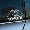 Elegantná nálepka na zadnom okne automobilu značky Toyota zobrazuje ruky formujúce tvar srdca. Tento biely, moderný dizajn vyniká na tmavom pozadí skla a dodáva vozidlu jedinečný a osobný dotyk. Perfektný doplnok pre majiteľov áut Toyota, ktorí chcú vyjadriť svoju lásku k tejto značke a zároveň hľadajú kreatívne a estetické dekorácie na svoje vozidlo. Ideálna voľba pre milovníkov áut, ktorí túžia ozdobiť svoje auto štýlovým a jedinečným prvkom.