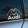 Plotrovaná nálepka s nápisom Audi a motívom rúk formujúcich srdce, jednoduchý a štýlový dizajn pre fanúšikov značky.