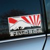 Štýlová nálepka na auto zobrazujúca horu Fudži s ikonickými červenými lúčmi vychádzajúceho slnka, symbolizujúcimi japonský motív. Dizajn je ladený do bielej, čiernej a červenej, čo vyniká na tmavom okne vozidla. Japonský text pod ilustráciou pridáva autentický nádych a robí z nálepky ideálny doplnok pre milovníkov Japonska a jeho kultúry. Táto kvalitná nálepka dokonale ozdobí bočné okno či kufor auta a dodá mu jedinečný vzhľad.