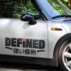 Moderná nálepka na dverách strieborného auta Mini Cooper s výrazným nápisom „DEFINED“, doplneným o malé červené srdce nad písmenom „i“. Pod anglickým textom sa nachádza japonský výraz „強い情熱“, čo znamená „silná vášeň“. Táto štýlová nálepka dodáva autu jedinečný vzhľad a vyjadruje energiu, odhodlanie a vášeň majiteľa. Perfektný doplnok pre tých, ktorí chcú zvýrazniť svoj osobný štýl prostredníctvom auta.