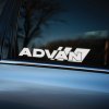 Plotrovaná nálepka na auto s logom ADVAN, dynamický dizajn s nakloneným písmom a výrazným geometrickým prvkom za textom.