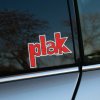 Plotrovaná nálepka na auto s logom Plak, červený retro nápis s bielym obrysom a dynamicky zalomeným písmom.