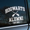 Plotrovaná nálepka na auto s nápisom „Hogwarts Alumni“, prekríženými metlami a textom „EST 993“ v štýle fanúšikov Harryho Pottera.