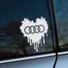 Plotrovaná nálepka na auto v tvare srdca s efektom stekajúcej farby, v strede doplnená o ikonické štyri kruhy Audi ako symbol lásky k značke.