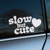Plotrovaná nálepka na auto s nápisom „slow but cute“ v retro písme a motívom srdca ako hravým doplnkom.