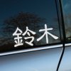 Elegantná nálepka na auto s japonskými znakmi 鈴木 (Suzuki), umiestnená na zadnom okne šedého automobilu. Táto štýlová dekorácia dokonale zvýrazní vašu lásku k japonskej značke a pridá vášmu vozidlu osobitý vzhľad. Vyberte si kvalitné auto nálepky pre váš Suzuki a vylepšite jeho dizajn.