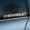 Nálepka s nápisom „Chevrolet“ umiestnená na zadnom bočnom skle automobilu. Moderný dizajn bieleho písma výrazne kontrastuje s tmavým sklom, čo vytvára štýlový a športový vzhľad vozidla. Táto nálepka je ideálnym doplnkom pre majiteľov Chevroletov, ktorí chcú zdôrazniť značku svojho auta a pridať mu osobitý charakter.