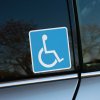 Tlačená nálepka s modrým symbolom osoby na invalidnom vozíku, vhodná na označenie vozidiel pre osoby so zdravotným postihnutím.
