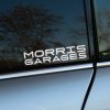 Plotrovaná nálepka s textom „Morris Garages“ v dvojriadkovom futuristickom fonte. Štýlový doplnok pre nadšencov značky MG.