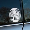 Plotrovaná nálepka s ikonickým japonským symbolom daruma, výrazná tvár a znak pre „šťastie“ v tradičnom štýle.