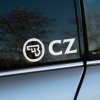 Plotrovaná nálepka na auto s logom CZ, moderný kruhový emblém so zbraňovým motívom a výrazným skratkovým nápisom vedľa.