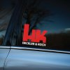 Plotrovaná nálepka na auto s dvojfarebným logom Heckler & Koch, výrazné iniciály HK a nápis v modernom technickom štýle.