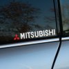 Plotrovaná nálepka na auto s malým červeným logom Mitsubishi a bielym nápisom značky v modernom bezpätkovom písme.
