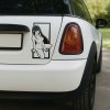 Plotrovaná nálepka na auto so siluetou anime dievčaťa s dlhými vlasmi v sediacej póze, umiestnenou v jednoduchom ráme.