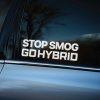 Plotrovaná nálepka s dvojriadkovým nápisom STOP SMOG GO HYBRID vo veľkých bielych písmenách, určená na podporu ekologickej dopravy.