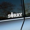 Plotrovaná nálepka s nápisom SORRY, kde písmeno O tvorí kreslená ruka s prostredníkom vztýčeným nahor v humornom štýle.