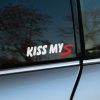 Plotrovaná nálepka s nápisom v oblom fonte, ktorú uzatvára výrazne pretiahnuté a dravé písmeno s textom KISS MY S.