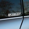 Plotrovaná nálepka s dynamickým dvojriadkovým nápisom v presnom textovom znení SKYACTIV TECHNOLOGY s ostrými hranami.