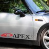 Plotrovaná nálepka na auto s logom APEXi, biely nápis doplnený výrazným červeným oblúkovým symbolom vľavo.