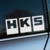 Biela nálepka „HKS“ s odvážnym a geometrickým dizajnom, kde sú písmená umiestnené v samostatných štvorcoch, nalepená na tmavom bočnom okne auta. Tento ikonický štýl odráža renomé značky HKS, známej v oblasti vysokovýkonných automobilových dielov a tuningu. Kontrast medzi ostrým bielym logom a tmavým sklom zaručuje jeho viditeľnosť, zatiaľ čo strieborná karoséria vozidla pridáva na elegancii. Ideálne pre tuningových nadšencov a fanúšikov automobilového výkonu, ktorí chcú svojmu vozidlu dodať športový charakter. Kľúčové slová: nálepka HKS, tuning doplnky, vysokovýkonné diely, nálepky na auto, personalizácia vozidla.