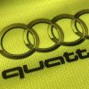 Detail potlače na reflexnej veste s logom quattro, čierne písmo pod prepojenými kruhmi na žltom polyesterovom textile.