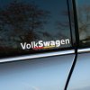 Plotrovaná nálepka s nápisom „Volkswagen“ a nemeckou trikolórou pod textom na bočné okno auta.