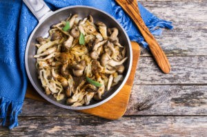 Fried oyster mushrooms with onions and spices in a plate on a wooden background. Selective focus.