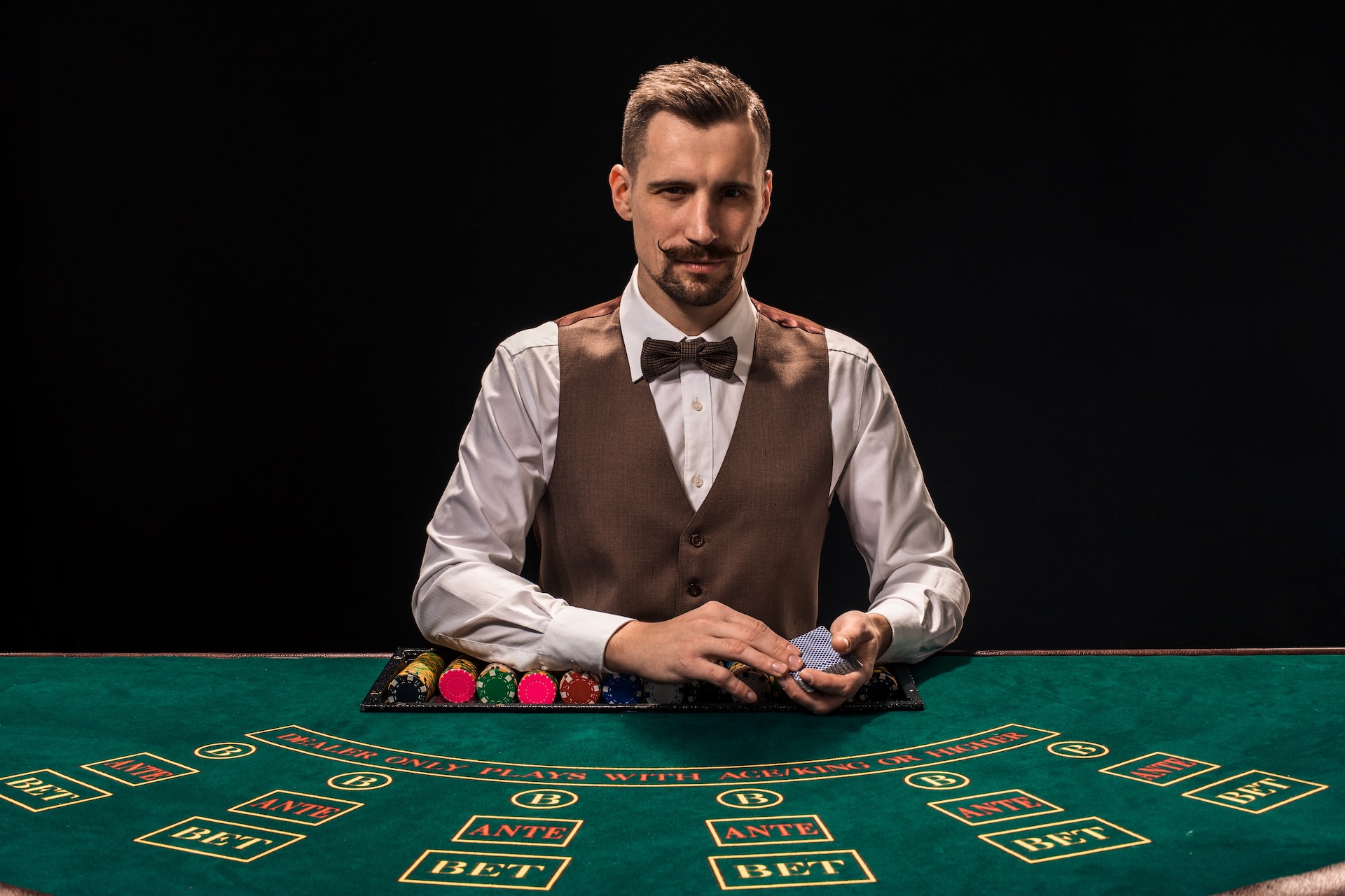 portrait-croupier-is-holding-playing-cards-gambling-chips-table-black-background-young-male-croupier-shirt-waistcoat-bow-tie-is-waiting-you-blackjack-table