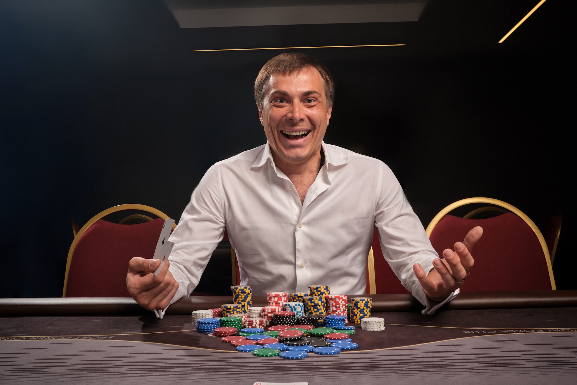 young-smiling-man-white-classic-shirt-is-playing-poker-sitting-table-casino-he-is-rejoicing-winning-looking-camera-gambling-money-games-fortune