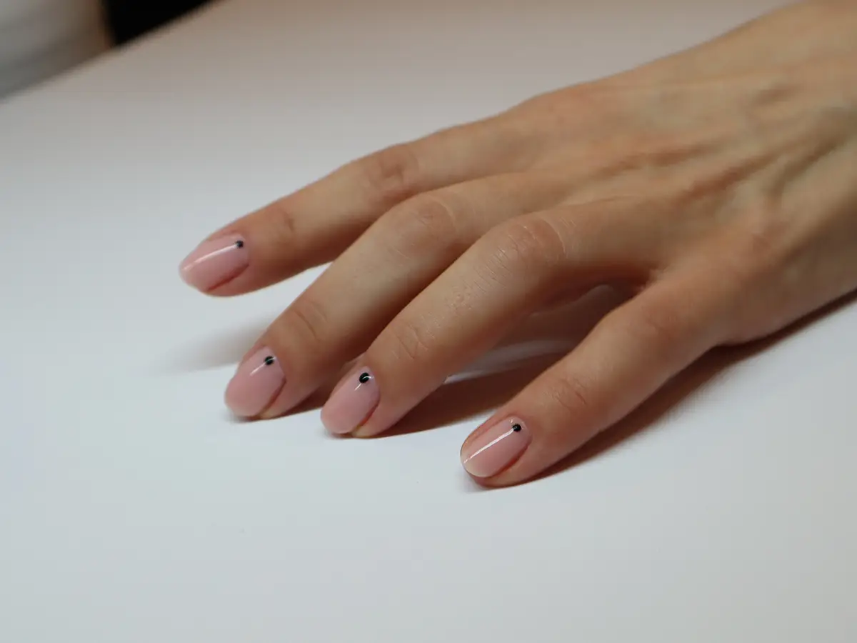 Manikúra v Praze: Ženská ruka na stole s krásnou nude manikúrou s růžovými nehty s černou tečkou.