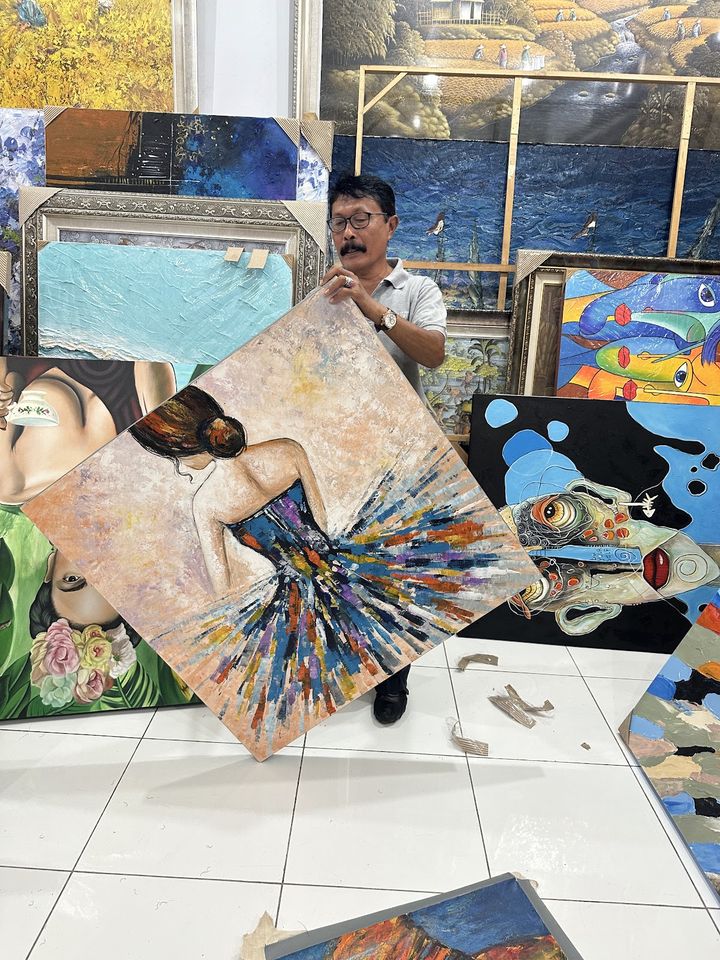 Pracovník galerie drží abstraktní obraz tanečnice mezi dalšími plátny