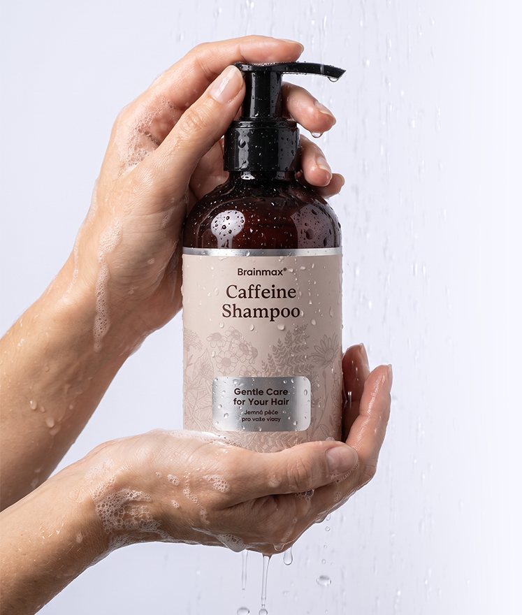 Ruce s pěnou svírají lahev Brainmax Caffeine Shampoo