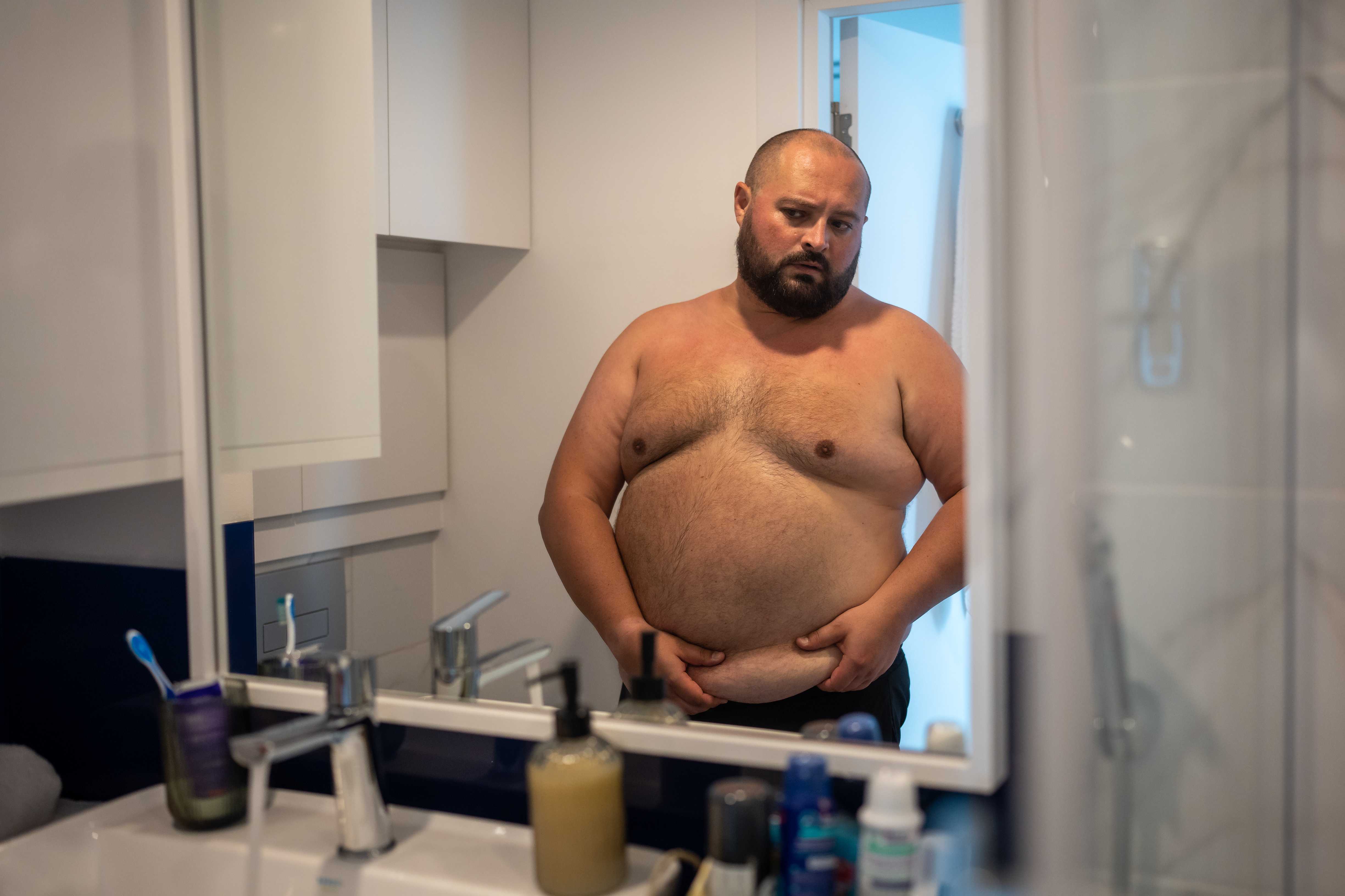 oversize-man-touch-sagging-belly-in-front-of-mirro-2023-11-27-05-02-52-utc_11zon