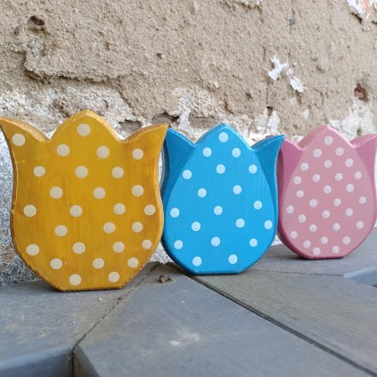 tři dřevěné tulipány s bílými puntíky v barvách modrá, okrová, růžová, foto na dřevěném podkladu před starou zdí