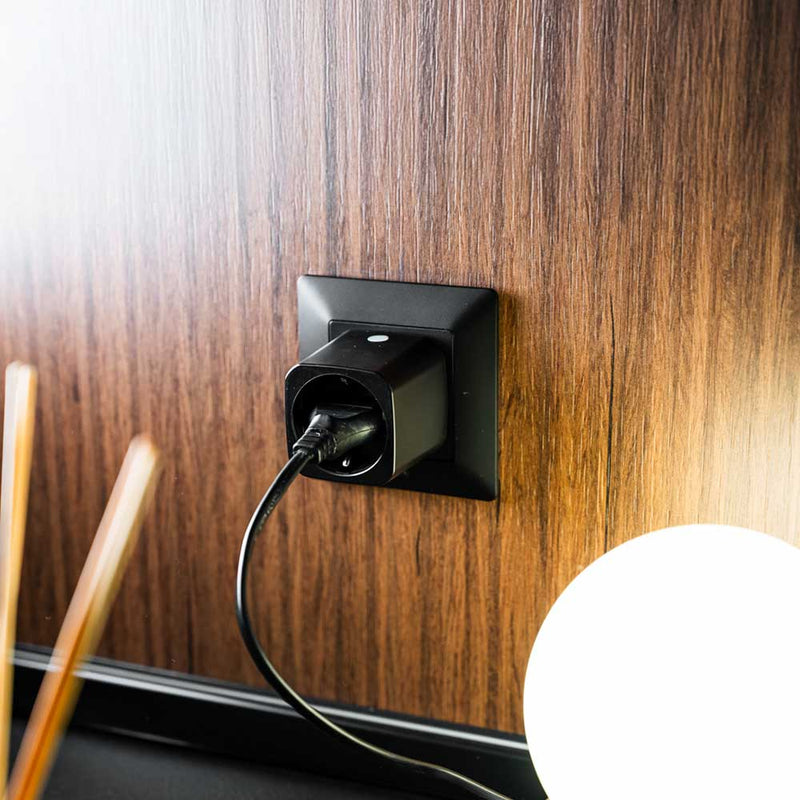 Instalovaná zásuvka Shelly Plug M Gen3 v černém provedení zapojená do dřevěného obložení zdi