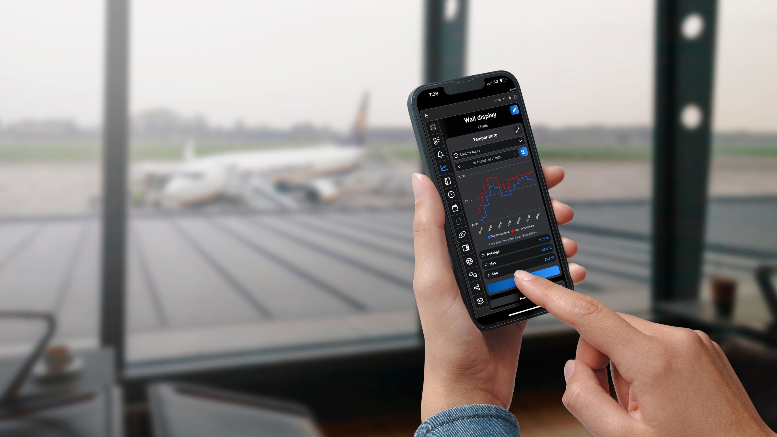 Ruka drží telefon s aplikací Shelly Smart Control zobrazující graf minimální a maximální teploty zařízení Wall display za posledních 24 hodin