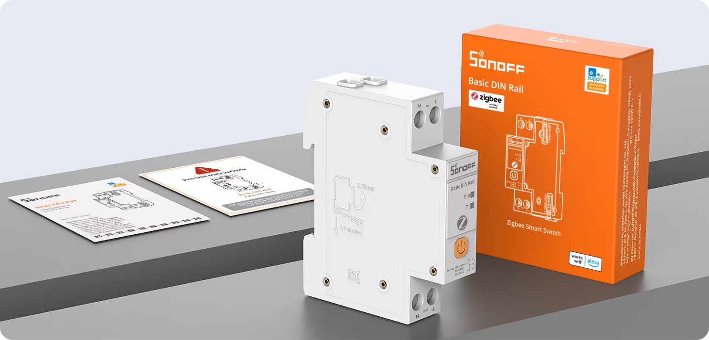 Spínač BASIC-ZB1GSP položený vedle oranžové krabice Basic DIN Rail Zigbee Smart Switch a přiložených návodů