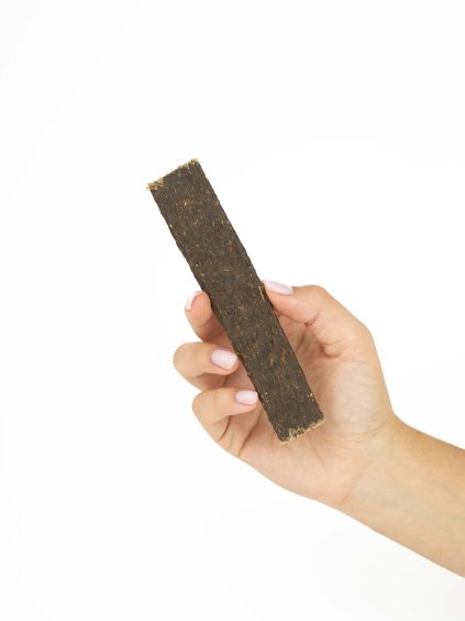 Ruka drží jeden masný plátek z jeleního masa Panakei pro psy na bílém pozadí.