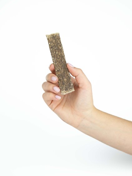 Ruka drží jeden masový plátek ze srnčího masa Panakei pro psy na bílém pozadí