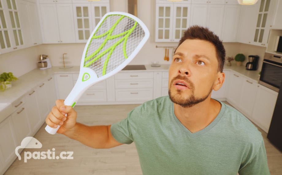 muž loví mouchy v kuchyni s elektrickou plácačkou