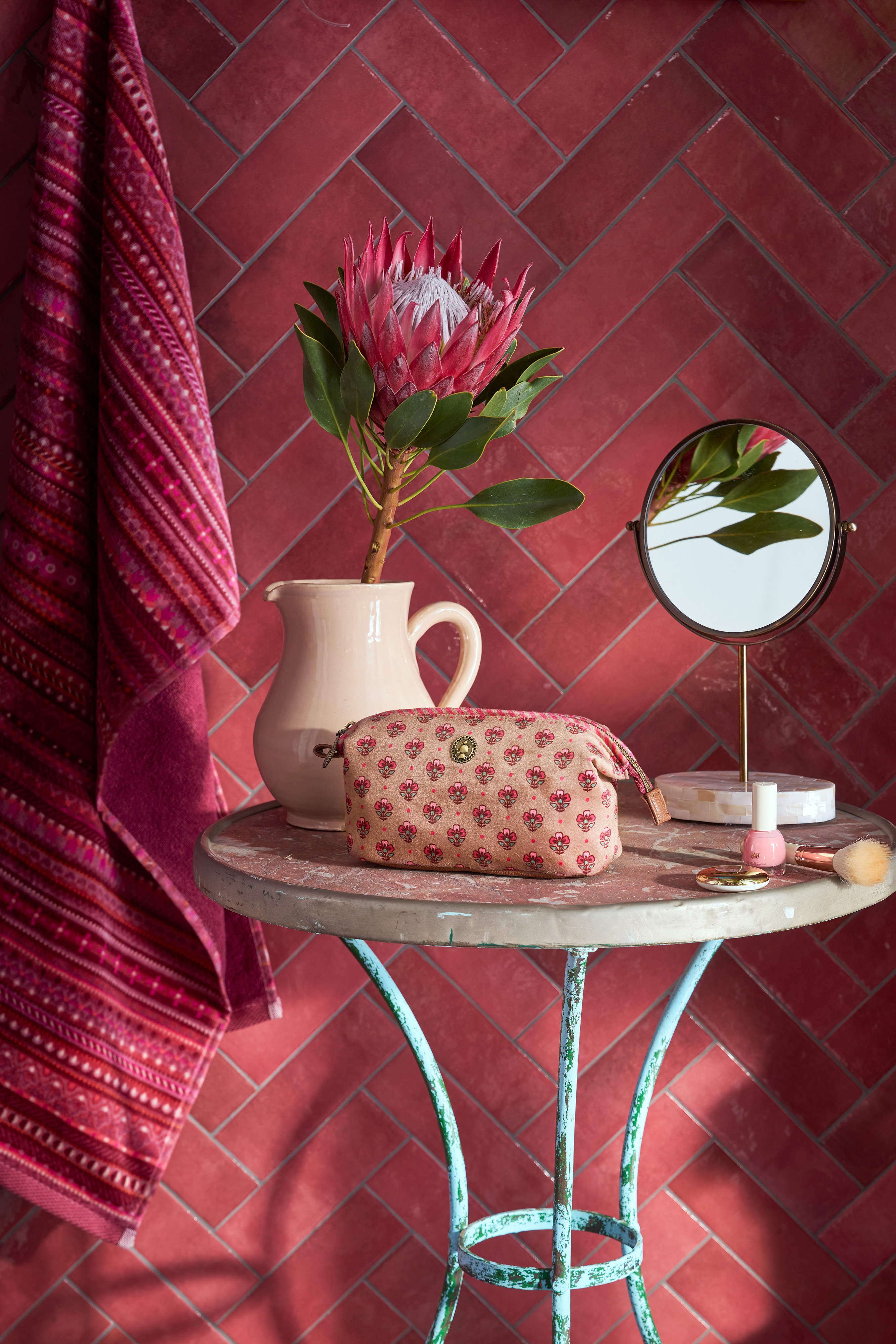 atmosférické foto Pip Studio kosmetická taška Cooper Jaipur Flower, růžová na kovovém stolku vedle vázy s velkou kytkou a stojícím zrcátkem, vedle stolku je pověšený ručník v tmavě růžové barvě s proužkovaným vzorem s květinami