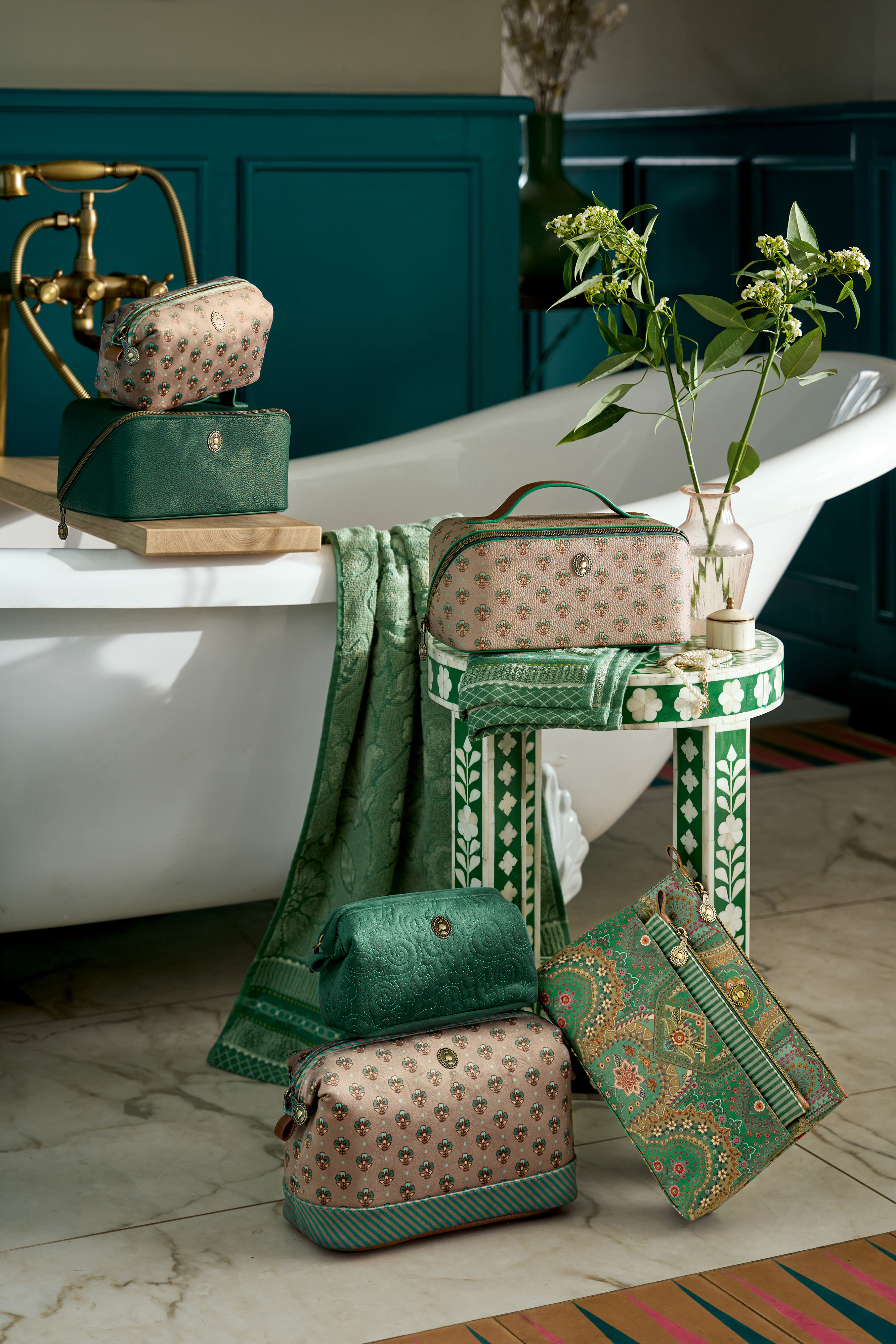 Atmosférické foto všech kosmetických taštiček a kufru z kolekce Pip Studio Jaipur flower v zelené a pískové barvě v designové koupelně , na zemi, na vaně , na designové stoličče v kombinaci se zelenými ručníky a osušky navíc s kosmetickou taštičkou dva v jednom z kolekce Jabali a etue Velvet Quilted malá