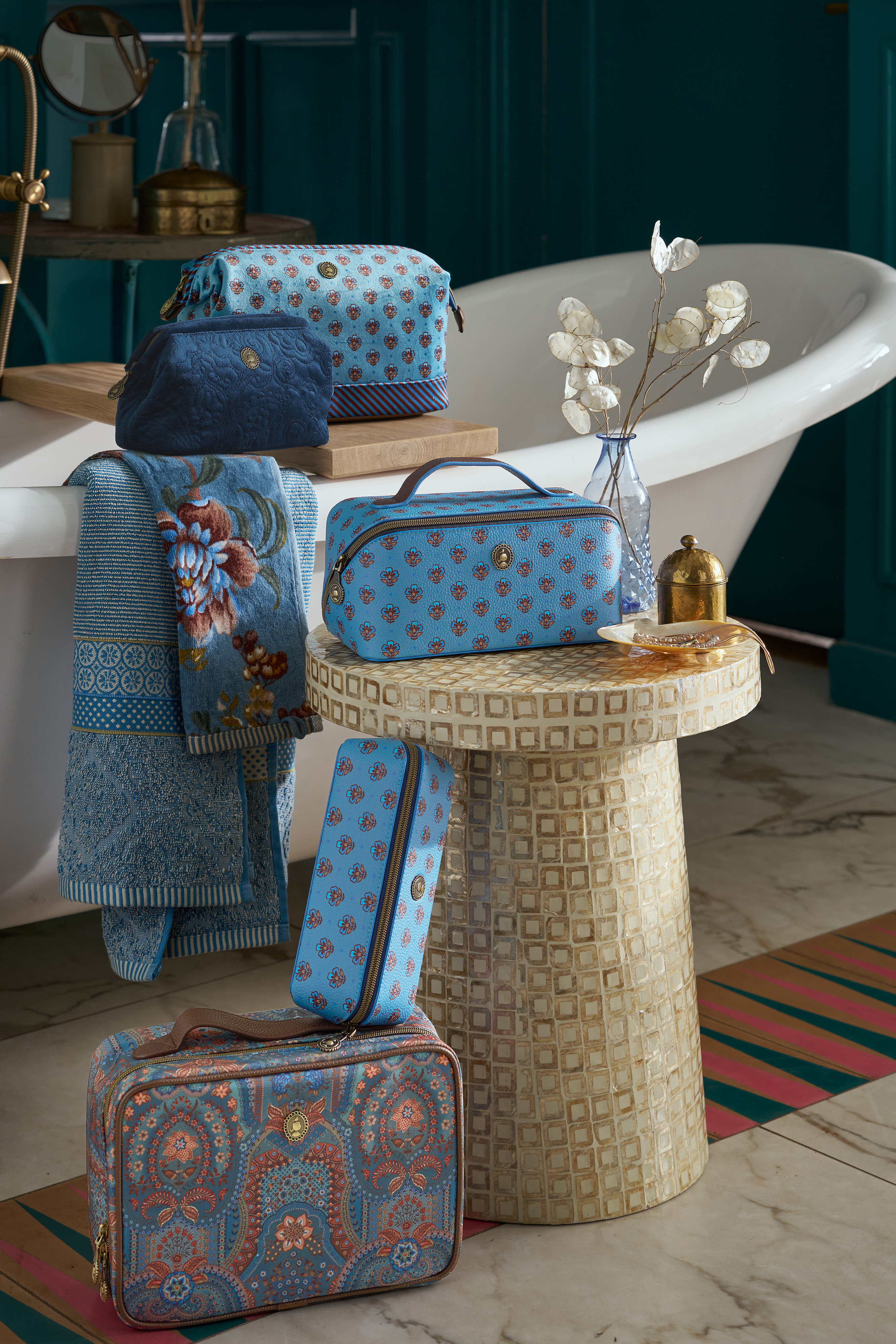 Kolekce sametových kosmetických tašek a cestovních kufříků Pip Studio z kolekce Jabali a Jaipur Flower Blue v sytě modré barvě u vany v designové koupelně.